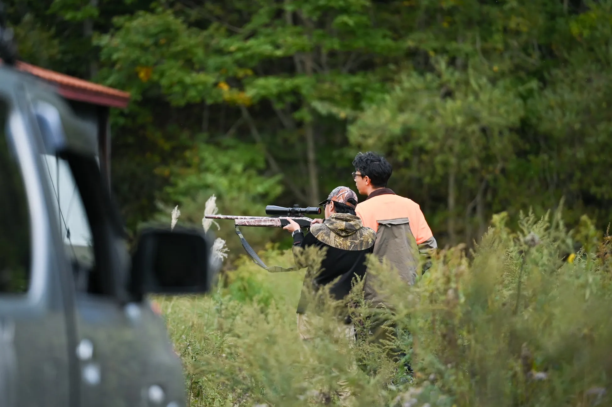 2人の男性が、ライフル銃を構えて草むらの中に立っている写真